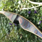 Ein Hybridbogen mit bunten, geschichteten Mustern, der auf grünem Gras und kleinen lila Blumen liegt.