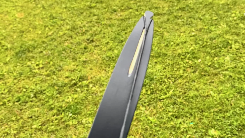 Ein verdrehter Wurfarm mit angelegter Sehne. Im Hintergrund eine Wiese.